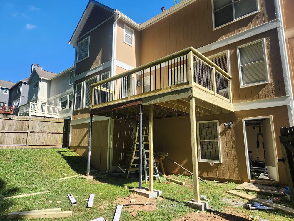 Raised deck with black metal balusters under construction on the back of a two-story house